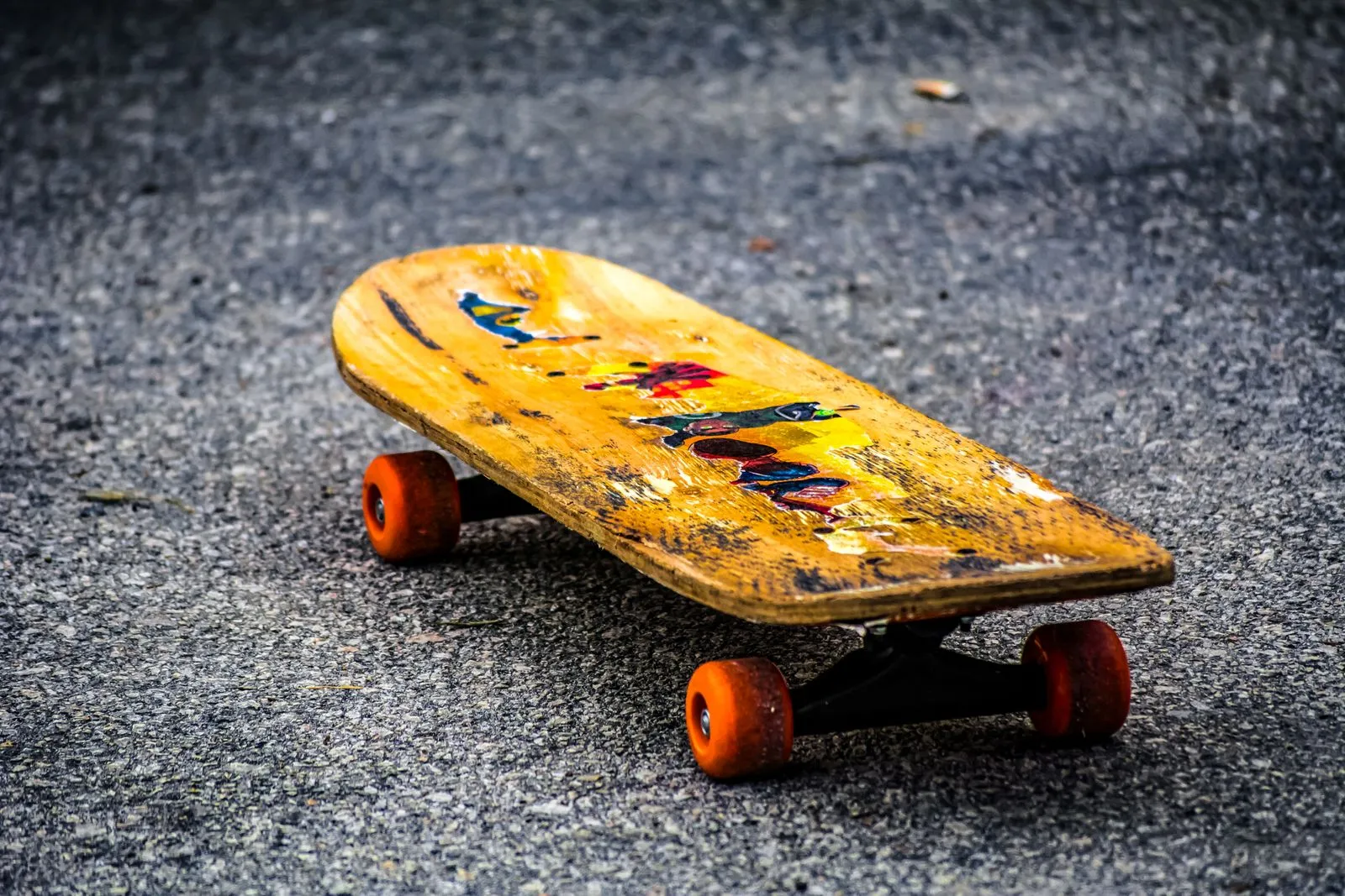 A vintage skateboard with a worn deck and colorful design lying on asphalt.